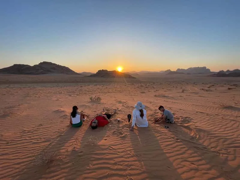 4x4 jeep crossing the red sand dunes of Wadi Rum desert in Jordan with towering sandstone cliffs in the background